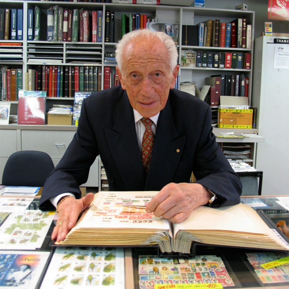 Max Stern, sitting at a desk, pair of tweezers in one hand, looking at a large stamp album