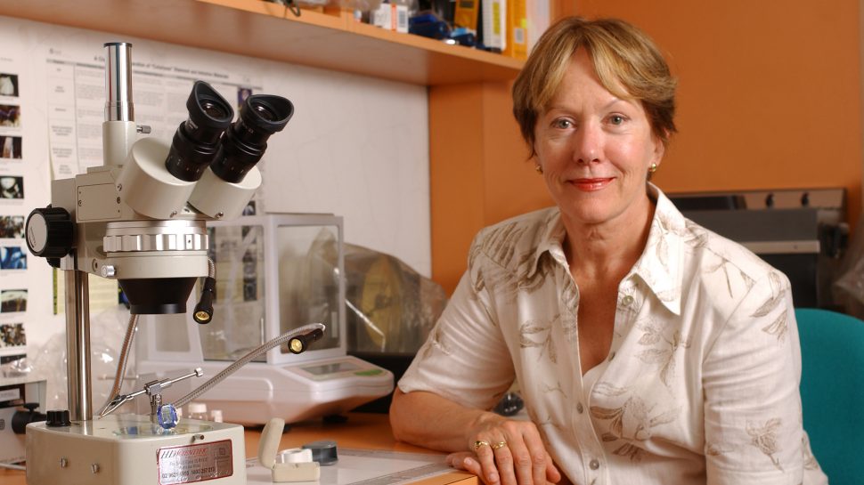 Photo of Gayle Sutherland in front a of desk containing a microscope