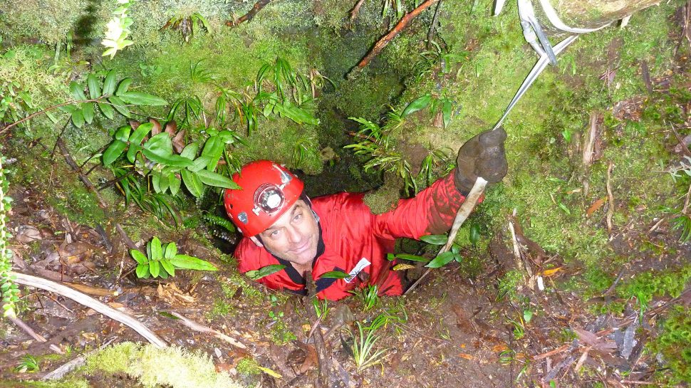 Stefan Eberhard dressed in red caving gear and helmet, peering out from a new cave